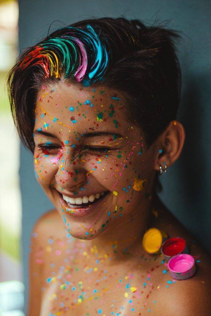 Une jeune femme souriante et éclaboussée de peinture.