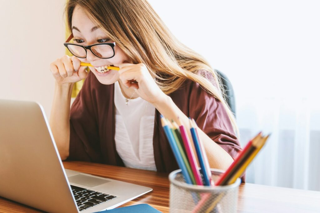 Une femme mordant un crayon alors qu'elle était assise sur une chaise devant un ordinateur pendant la journée.